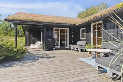 a black cottage with a deck with a thatched roof at BL1437-Blokhus-Berberisvej-78 in Blokhus