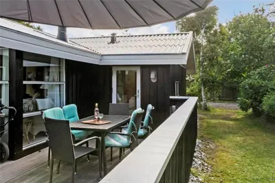 an outdoor deck with a table and chairs and an umbrella at BL226-Blokhus-Paa-Bakken-13 in Blokhus