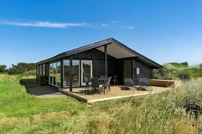 a black house with a deck and chairs in a field at BL1326-Saltum-Svendborgvej-19 in Saltum