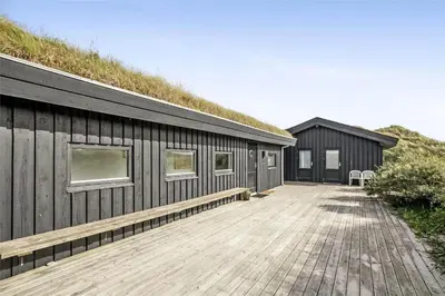 a building with a grass roof with a wooden deck at BL358-Pandrup-Kaskelotten-5 in Pandrup