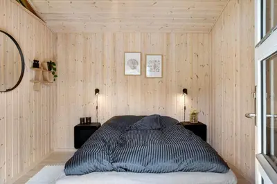 a bed in a room with wooden walls and two lamps at BL1313-Blokhus-Bag-Hojen-3 in Blokhus