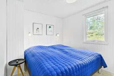 a white bedroom with a blue bed and a window at BL1585-Blokhus-Bregnehojvej-1 in Blokhus
