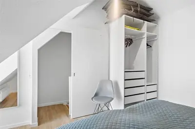 a bedroom with white walls and a bed and a chair at BL1584-Blokhus-Strandvejen-14-Lejl-4 in Blokhus