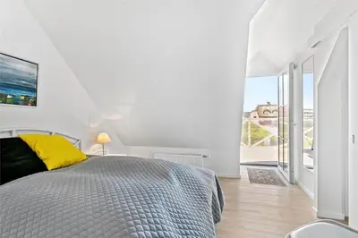 a white bedroom with a bed and a large window at BL1584-Blokhus-Strandvejen-14-Lejl-4 in Blokhus