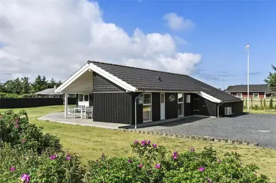 a black building with a table and chairs in a yard at BL1139-Blokhus-Sletten-3 in Blokhus