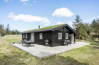 a black cabin with a deck with tables and chairs at BL1330-Blokhus-Risen-3 in Blokhus