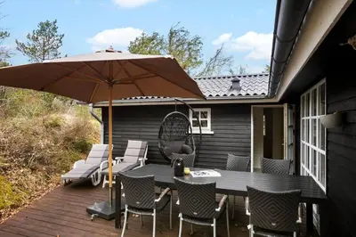 a wooden deck with a table and chairs and an umbrella at BL554-Blokhus-Kragebak-2 in Blokhus