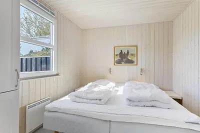 a bedroom with a bed with white sheets and a window at BL464-Blokhus-Blaabaerskraenten-8 in Blokhus
