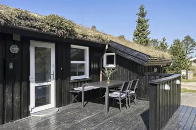 a black cabin with a table and chairs on a deck at BL464-Blokhus-Blaabaerskraenten-8 in Blokhus