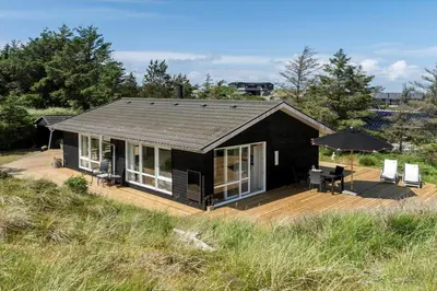 a black house with a deck and an umbrella at BL1371-Blokhus-Sletten-10-A in Blokhus