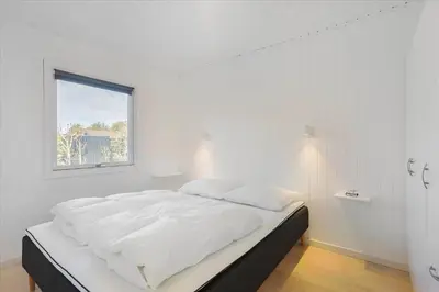 a white bedroom with a large bed with a window at BL1680-Blokhus-Klitgaardsvej-18 in Blokhus