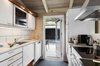 a kitchen with white cabinets and a door to a patio at BL485-Blokhus-Sandtoften-29 in Blokhus