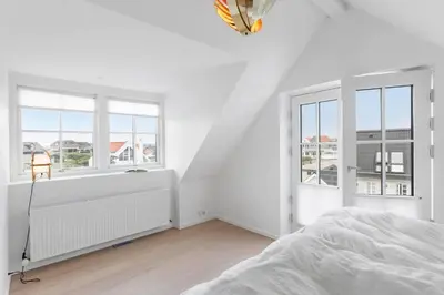 a white bedroom with a bed and two windows at BL1222-Blokhus-Strandvejen-13-B in Blokhus