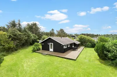 a black house with a deck in a yard at BL1218-Blokhus-Quintusvej-24 in Blokhus
