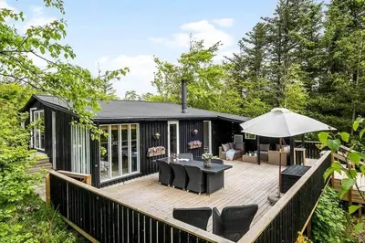 a black cabin with a deck with chairs and an umbrella at BL958-Blokhus-Havorns-Alle-14 in Blokhus