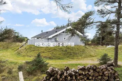 a house on top of a hill with a pile of logs at BL1329-Blokhus-Pirupshvarrevej-67 in Blokhus