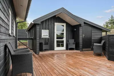a black house with a wooden deck with two chairs at BL1403-Blokhus-Sorensensvej-7 in Blokhus