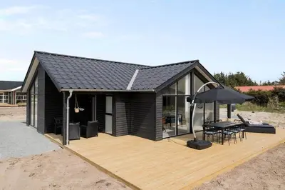 a black house with a deck with a table and an umbrella at BL1295-Saltum-Vesterhavs-Sletten-39 in Saltum