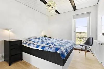 a bedroom with a bed and a chair and a window at BL1310-Blokhus-Moreavej-33-A in Blokhus