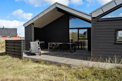a black house with a deck with a table and chairs at 332-Harboore-Hvilehjemsvej-20 in Harboør