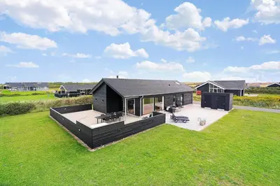 a black house with a deck in the grass at 237-Harboore-Neerlandiavej-17 in Harboør