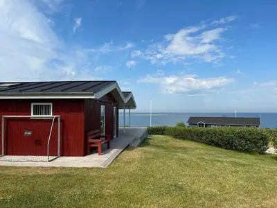 a red building with a bench in front of the ocean at G281-Lemvig-Syrenvej-81 in Lemvig