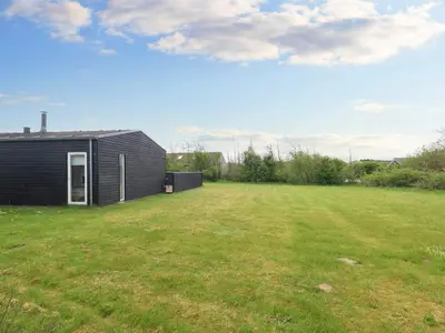 a black house in a field with a yard at Tranquil Retreat in Nature s Embrace-By Traum in Brovst