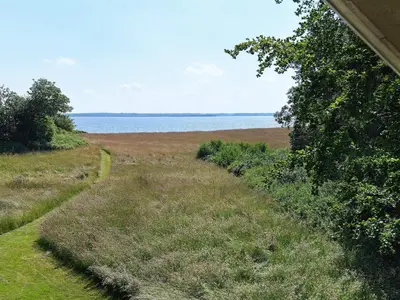 a field of grass next to a body of water at 6 person holiday home in Thyholm in Thyholm