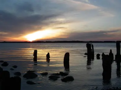 a sunset over a body of water with wooden posts at Luxury Retreat with Pool - By Traum Ferienwohnungen in Thyholm