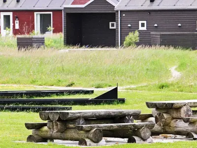 a group of logs in a field with a house at Holiday home for 24 guests, Brovst in Brovst