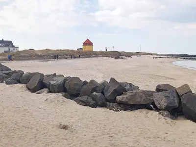 a pile of rocks on a beach with a building in the background at 6 person holiday home in Thyborøn-By Traum in Thyborøn