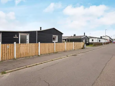 a black house with a fence next to a street at 5 person holiday home in Thyborøn in Thyborøn