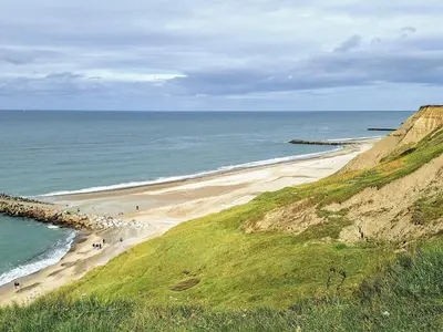 a beach with people walking on it next to the ocean at 6 person holiday home in Lemvig in Lemvig