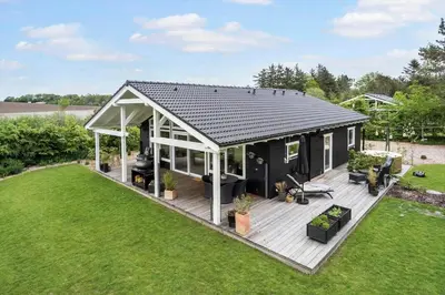 a black house with a deck in a yard at LF10058-Thyholm-Fyrrevej-17 in Thyholm
