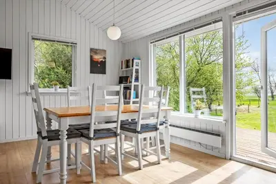 a dining room with a table and chairs and windows at LF13172-Nykobing-M-Strandvaenget-76 in Ejerslev