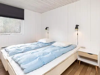 a bed with blue sheets in a room with a window at 6 person holiday home in Blokhus