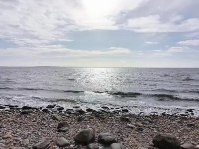 a rocky beach with the sun reflecting on the water at 6 person holiday home in Øster Assels in Øster Assels
