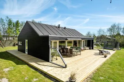 a black house with a wooden deck in a yard at JB215-Brovst-Kronvildtvej-194 in Brovst