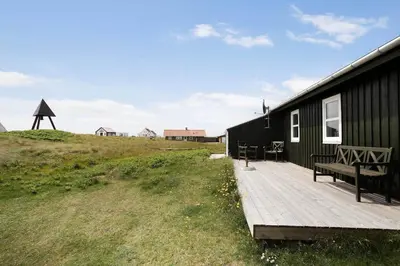 a black house with a wooden deck with a bench at JB109-Frostrup-Strandkaervej-8 in Frøstrup