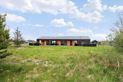 a house with a black roof in a field at JB141-Brovst-Kronvildtvej-86 in Brovst