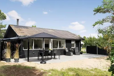 a black house with chairs and an umbrella at 1357-Snedsted-Grahavrevej-1 in Snedsted