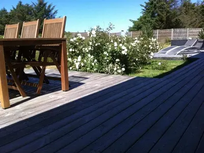 a wooden bench sitting on a deck with white flowers at Holiday home in Thisted with swimming pool in Thisted