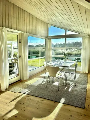 a dining room with a table and chairs and large windows at Bright Holiday Home Close To Sea Near Blokhus in Blokhus