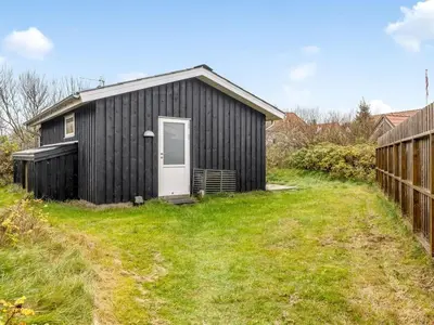 a black shed with a white door in a yard at Holiday Home Tekla - 75m from the sea by Interhome in Thisted