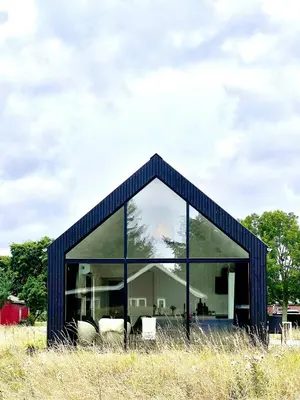 a black house with a large window in a field at Summer House Surrounded By Reeds Near Limfjorden in Lemvig
