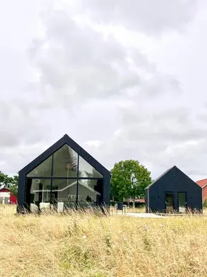 a black house with glass windows on a field at Summer House Surrounded By Reeds Near Limfjorden in Lemvig