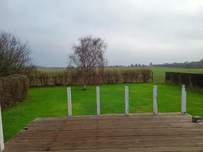 a field with a wooden deck and a field with trees at Bolig ved hav og fjord in Thyholm