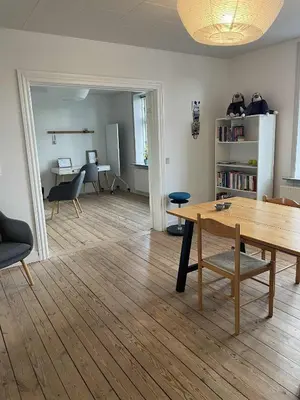 a living room with a wooden table and a desk at Lejlighed midt i Thisted in Thisted