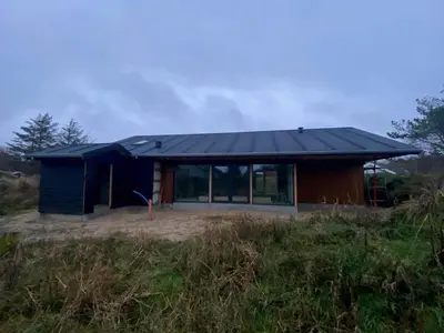 a house with a black roof on top of a field at BL1149-Blokhus-Paa-Bakken-12 in Blokhus