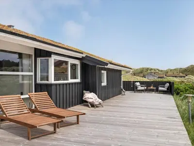 a wooden deck with two chairs and a house at Holiday Home Osfrid - 175m from the sea by Interhome in Blokhus